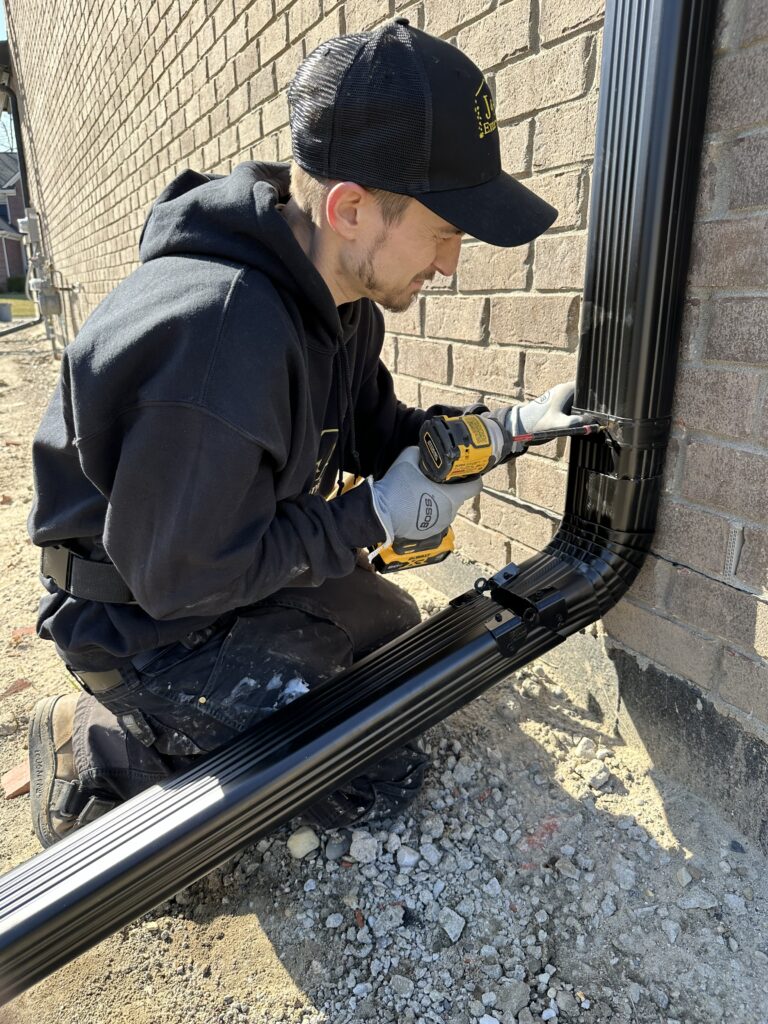 Black 3x4 6 inch gutter downspout being installed with hinges for easy mobility on a new build construction house in Richmond Michigan.