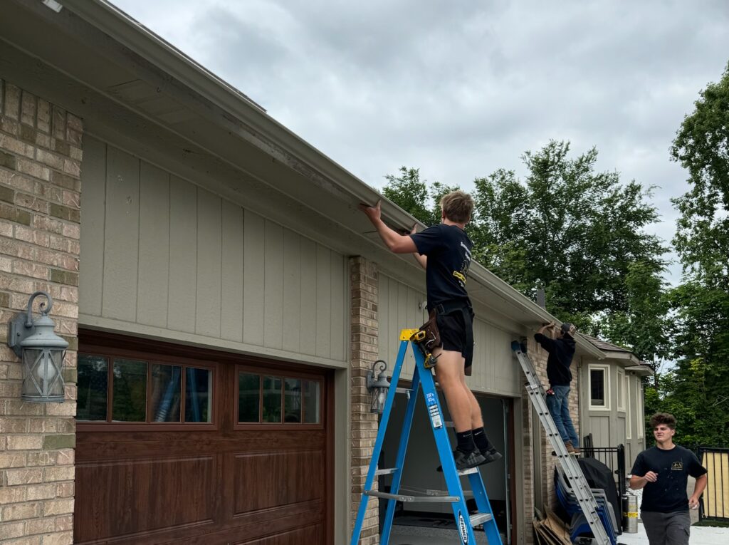 two men working on ladders on a brown brick home