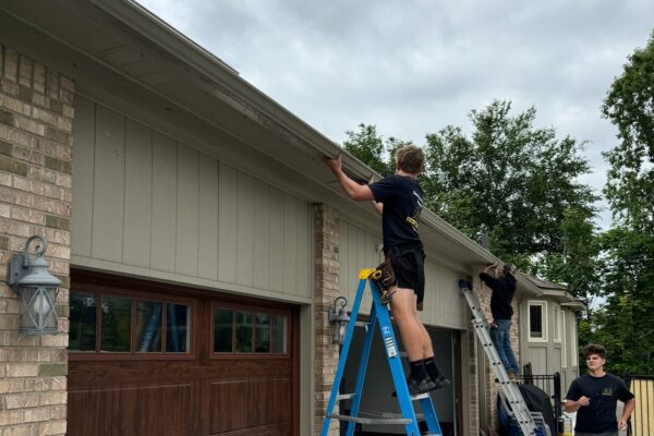 two men working on ladders on a brown brick home