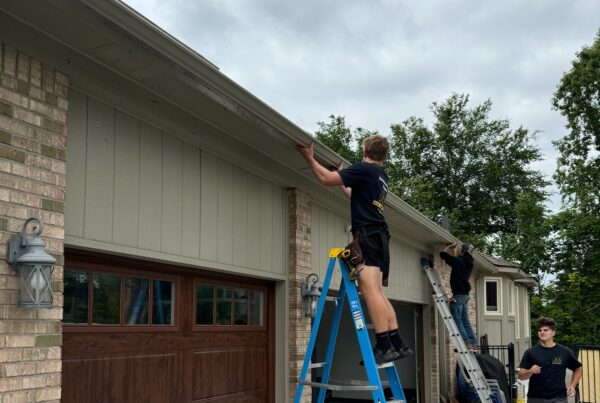 two men working on ladders on a brown brick home