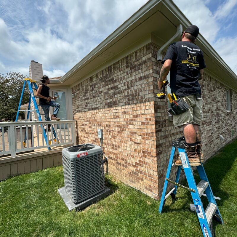 two men on ladders working on a brown brick home