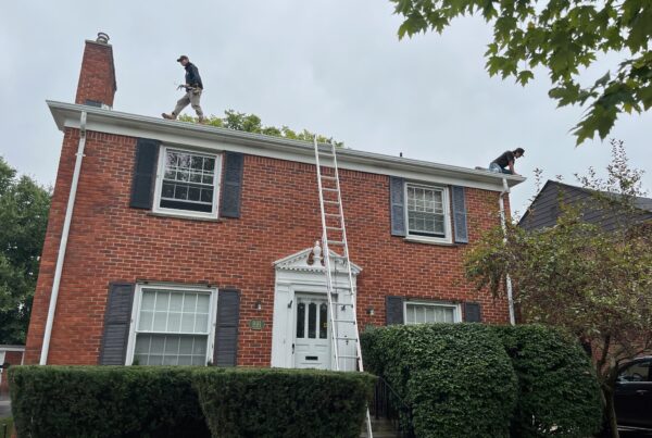 red brick home with men working on the roof using a ladder