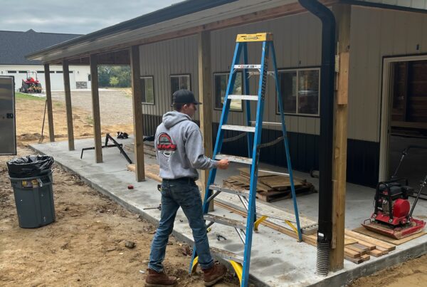 white siding home with black gutters, man working with ladder
