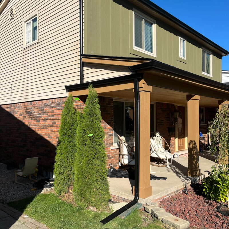 black gutters on a red brick home with green and beige siding