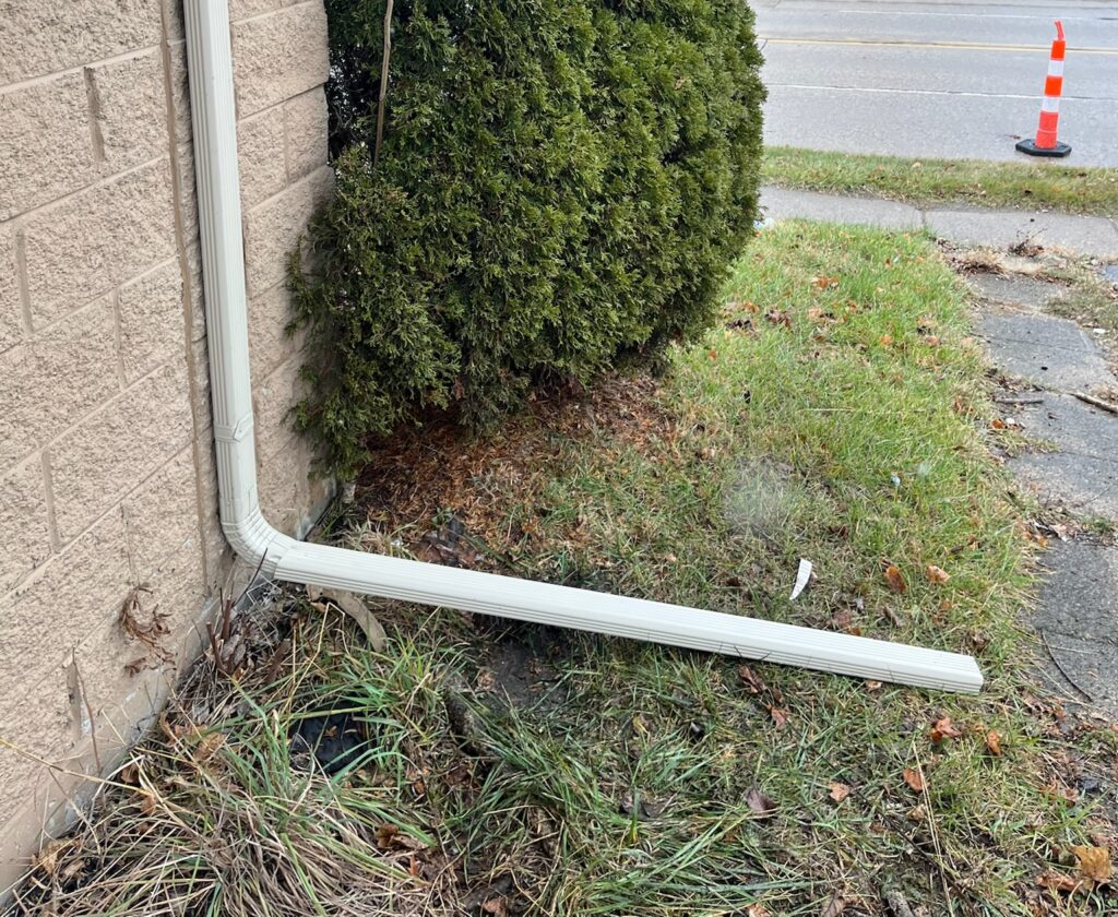 White gutter downspout on brown brick home with extension in grass