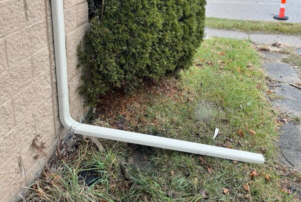 White gutter downspout on brown brick home with extension in grass