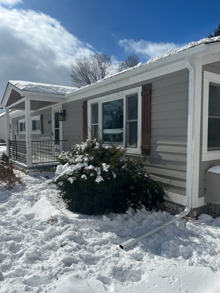 gray siding home with white gutters and snow