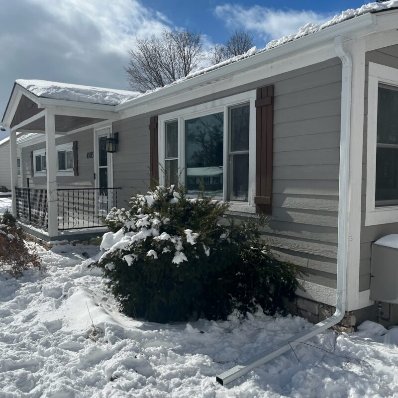 gray siding home with white gutters and snow