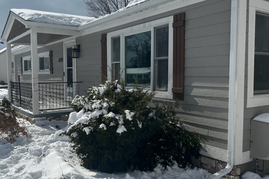 gray siding home with white gutters and snow