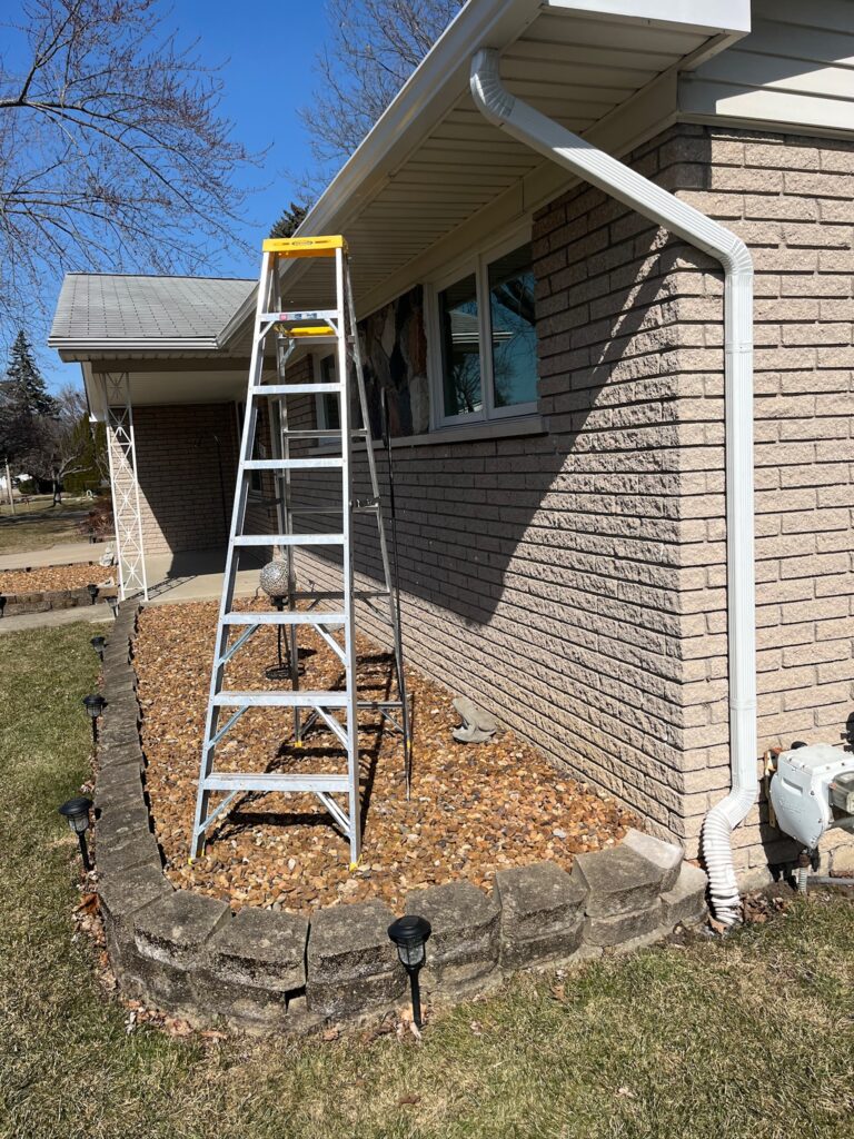 beige brick home with white downspout and a ladder